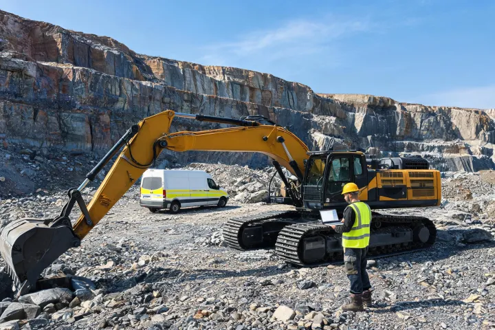 Field technician diagnosing excavator with laptop