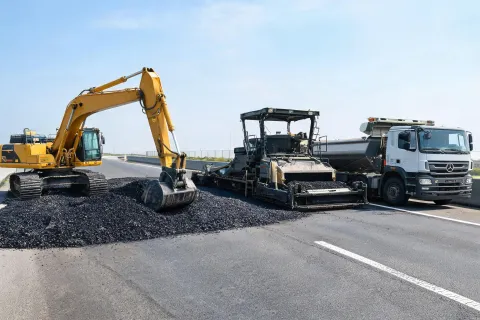 Excavator near asphalt paving train